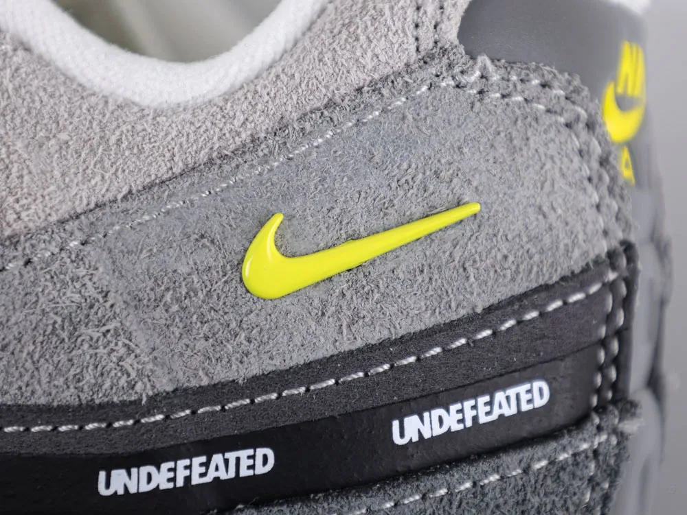 Close-up of gray suede sneaker with yellow logo and black leather stripe detail.
