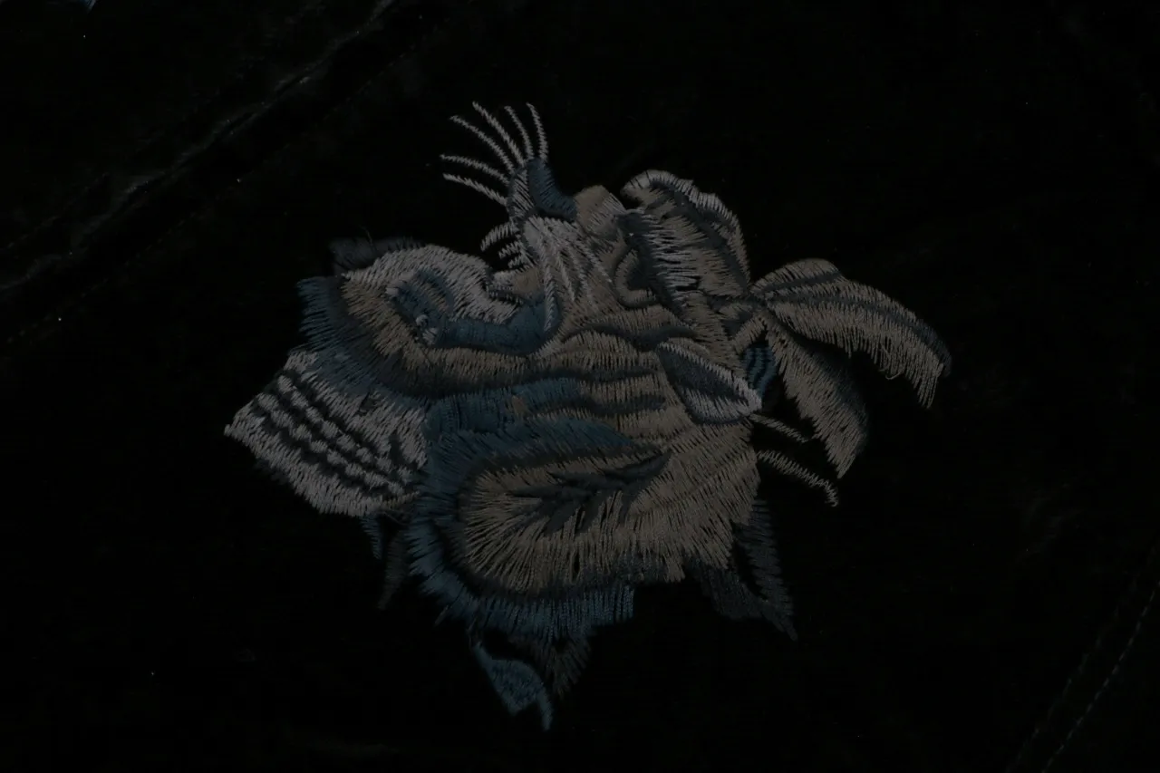 Dark embroidered fabric featuring intricate gray and blue stitch design on textile.