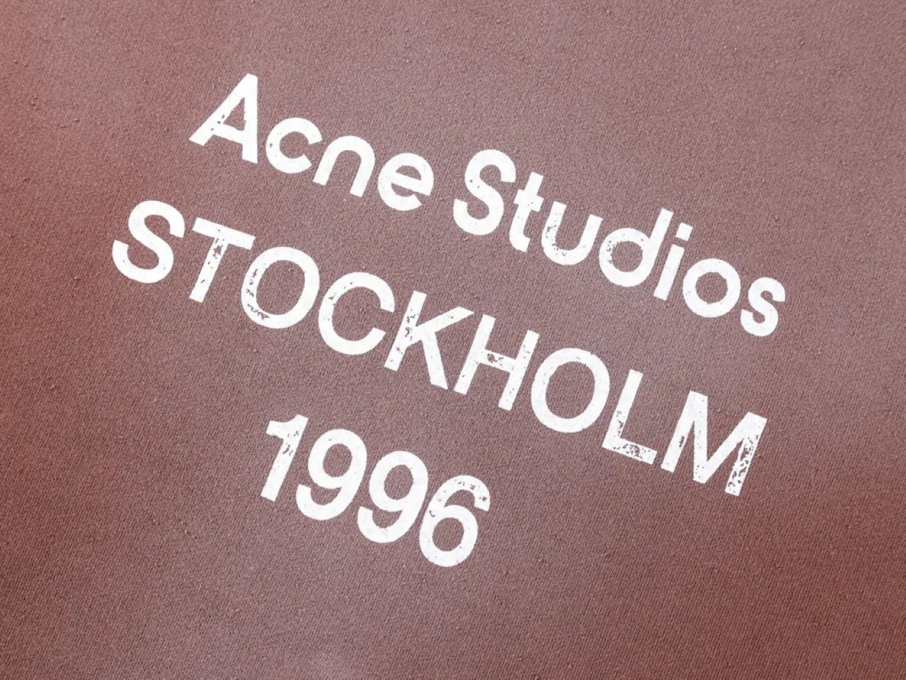 Brown fabric with white text print, featuring "Acne Studios Stockholm 1996."