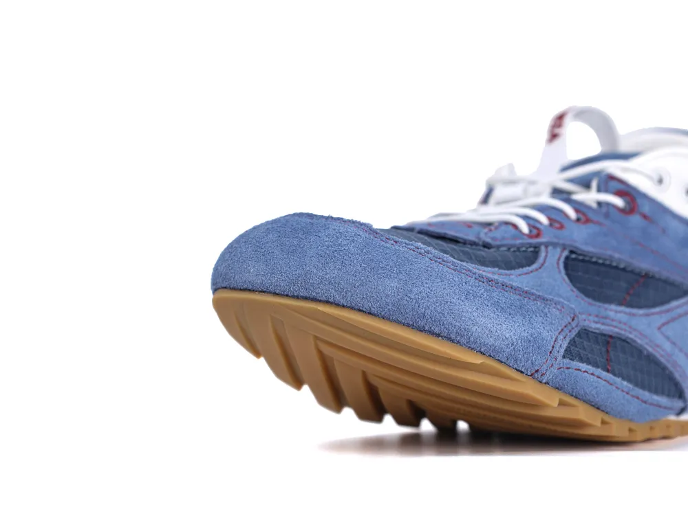 Close-up of blue suede shoe with brown rubber sole and white laces.