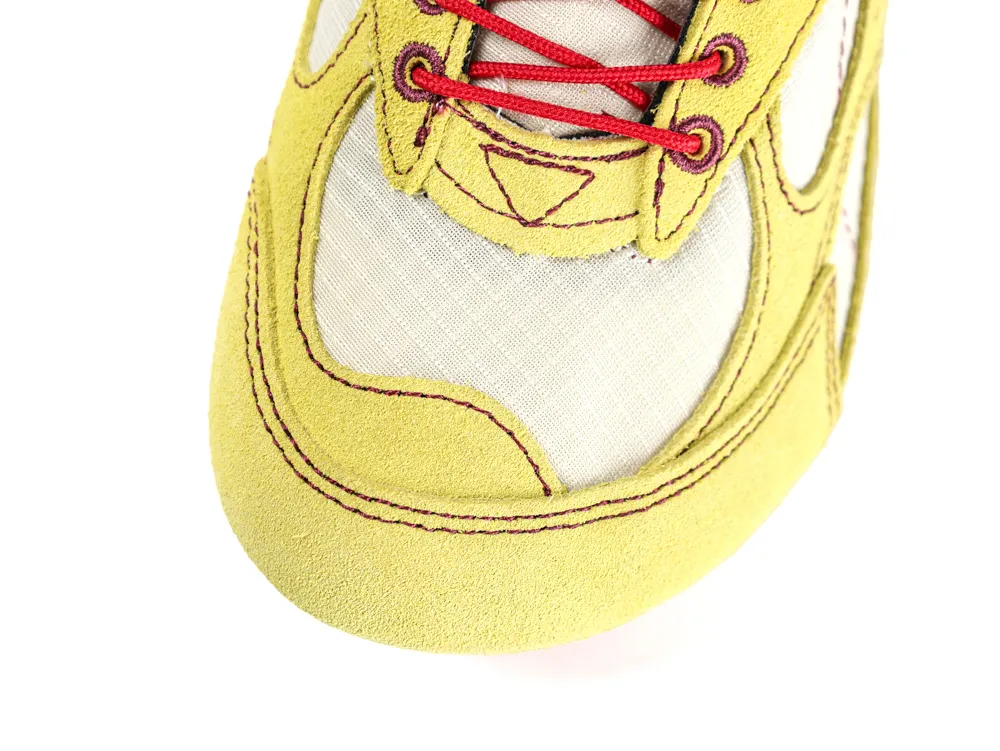 Close-up of yellow suede sneaker with red laces and beige fabric panel.