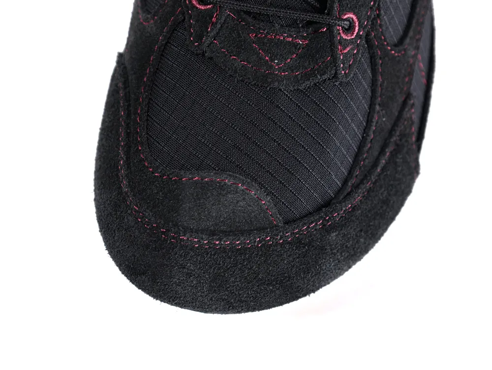 Black suede shoe with pink stitching and mesh fabric detail on toe area.