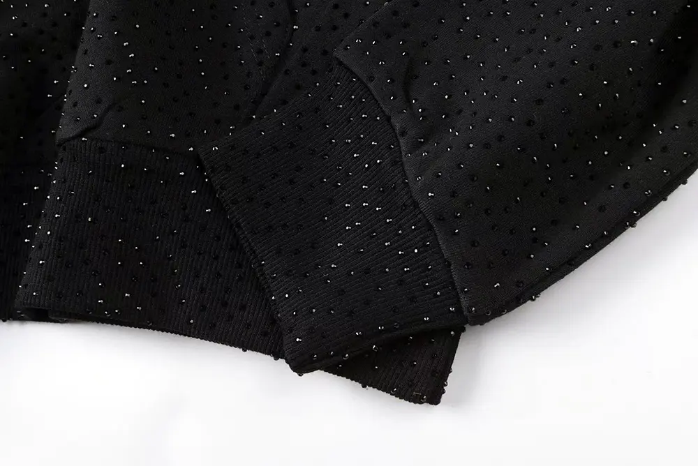 A top-down view of the sleeve of the Sp5der VVS Hoodie in Black, highlighting its cotton and polyester material and full rhinestone detailin