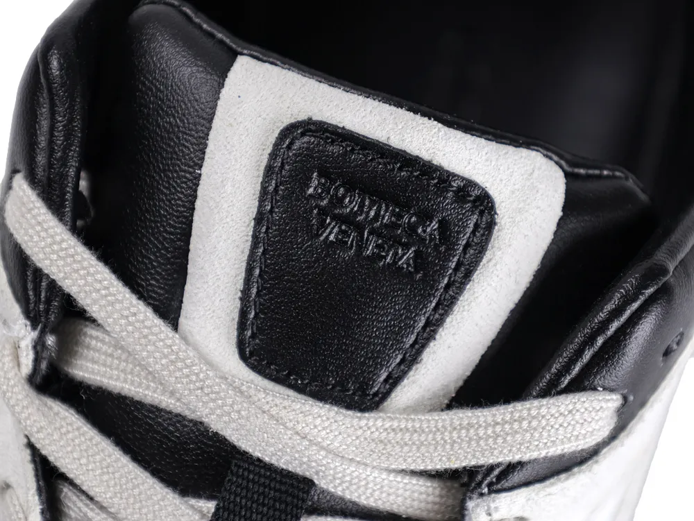 Black leather sneaker tongue with embossed text, surrounded by white suede and laces.