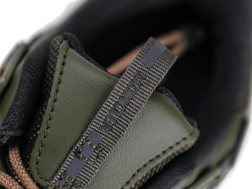 Close-up of a green leather shoe tongue, featuring brown laces and a textured, striped pull tab with stitched details.