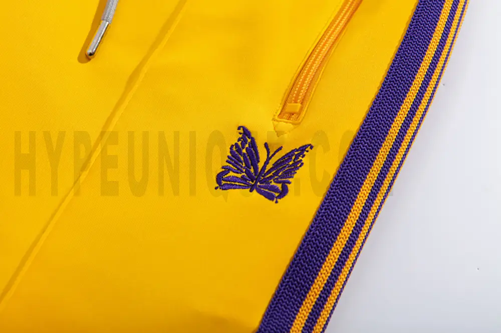 Close-up detail of the track pants pocket and delicate butterfly embroidery.