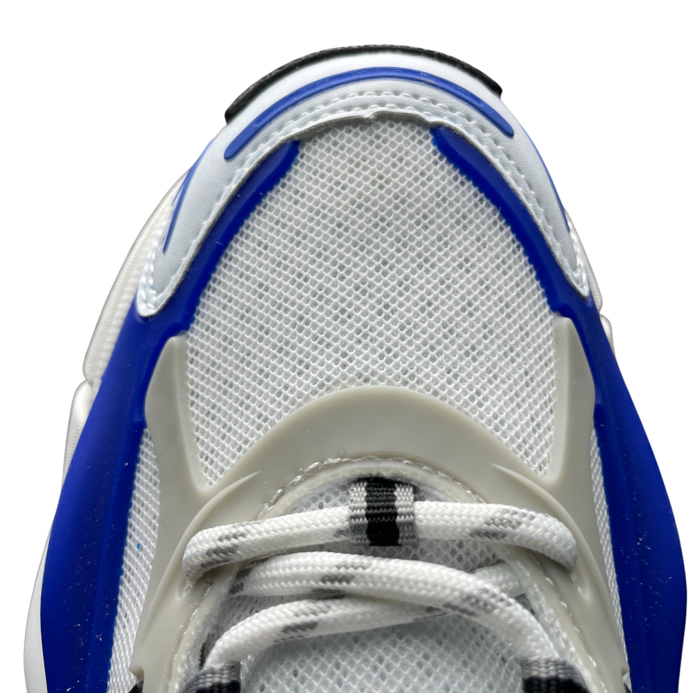 The image shows a sneaker sole with black textured rubber, white foam, and blue accents, highlighting various tread patterns.