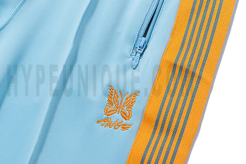 Close-up detail of the track pants pocket and delicate butterfly embroidery.
