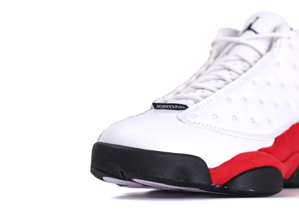White leather sneaker with red suede accents and black rubber sole details.
