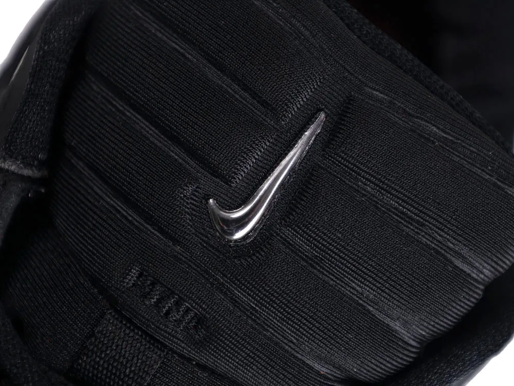 Close-up of a black fabric shoe tongue featuring a metallic logo.