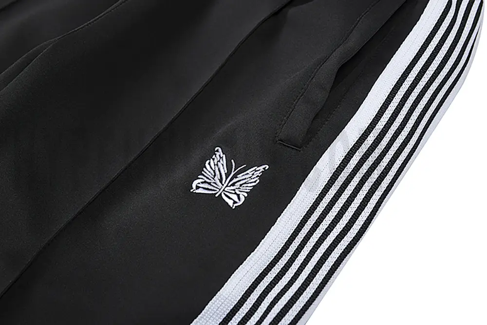 Detailed view of the pocket and intricate butterfly embroidery on the track pants.