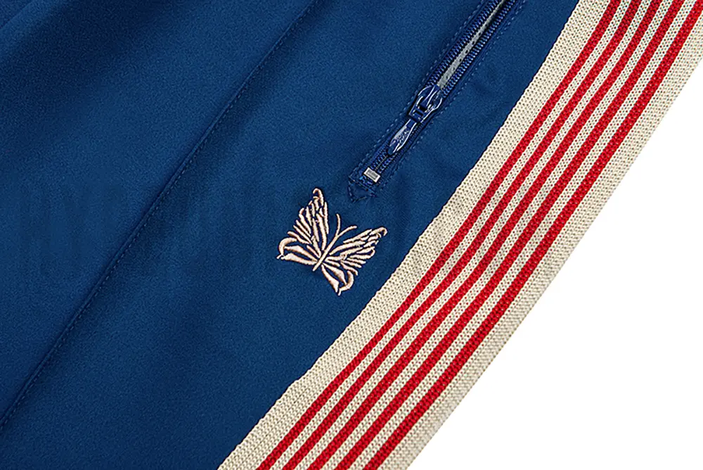 Close-up detail of the track pants pocket and delicate butterfly embroidery.