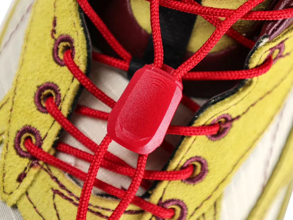 Close-up of a shoe with yellow suede, red laces, and plastic red toggle.