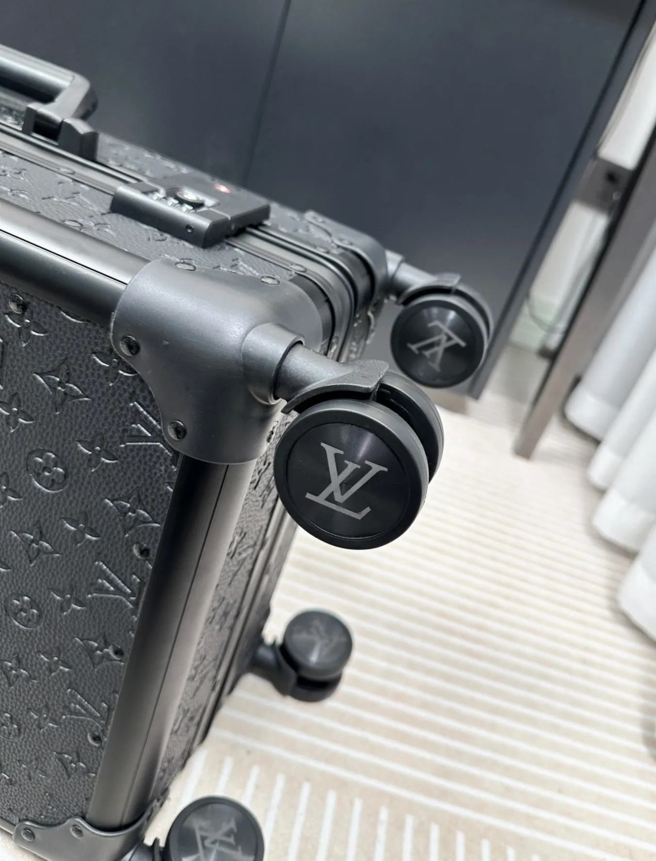 Black embossed monogram luggage spinner wheel detail