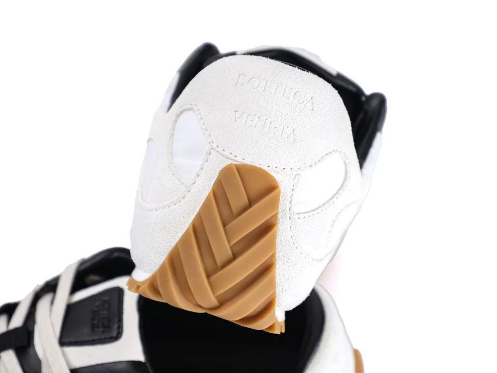 White suede shoe with brown rubber sole and black detailing.