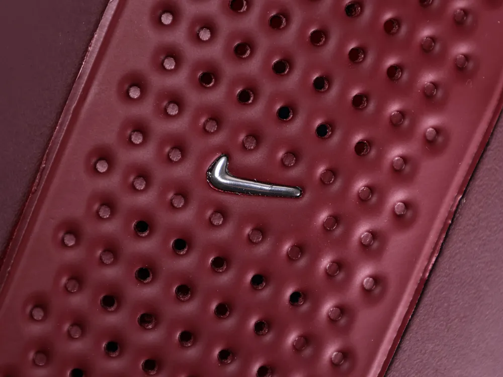 Close-up of a small silver Nike swoosh set into a perforated section of the burgundy upper.