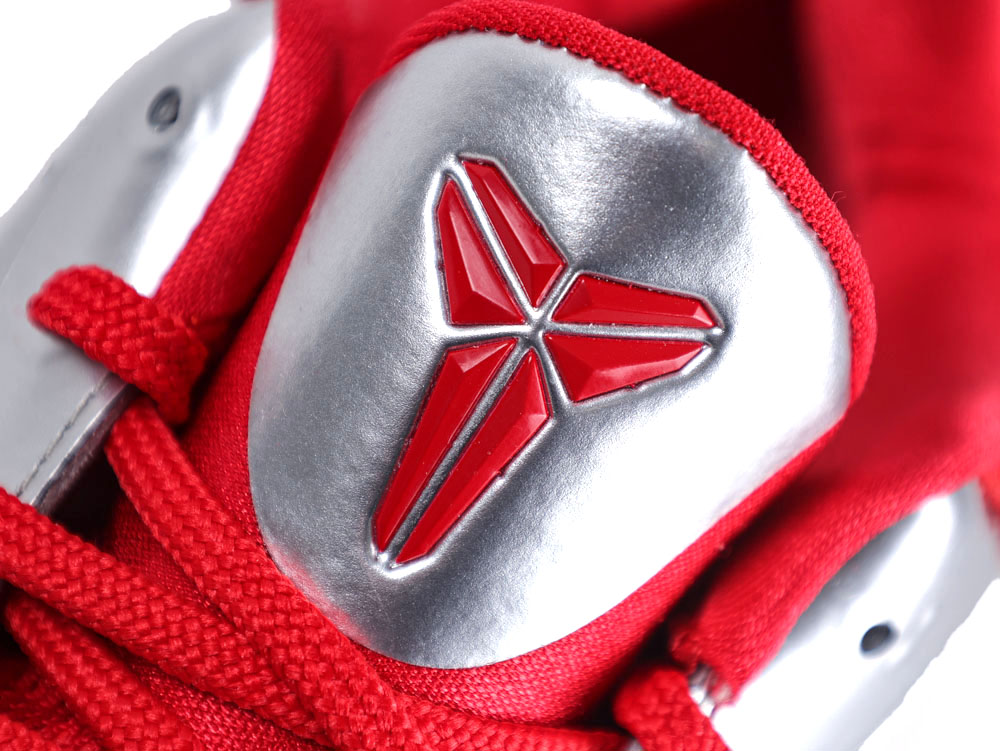 Close-up of a red and silver sneaker with a textured logo on the tongue.
