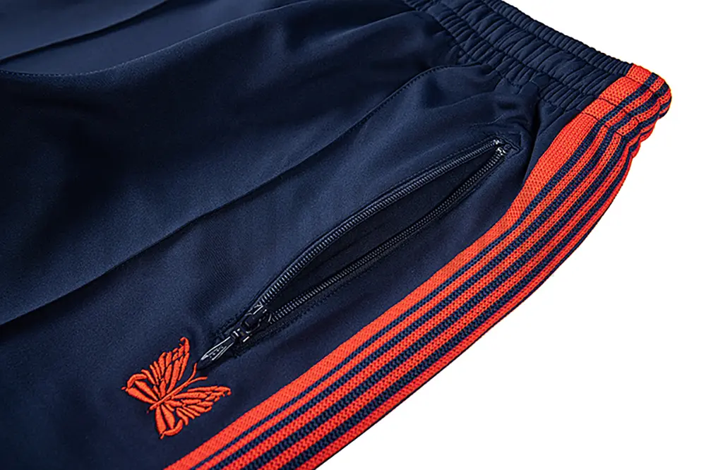 Close-up detail of the track pants pocket and delicate butterfly embroidery.