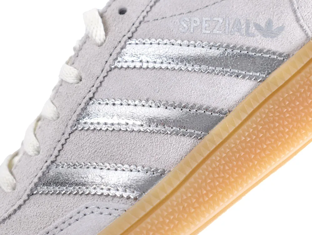 Close-up of gray suede sneaker with silver stripes and tan textured rubber sole.