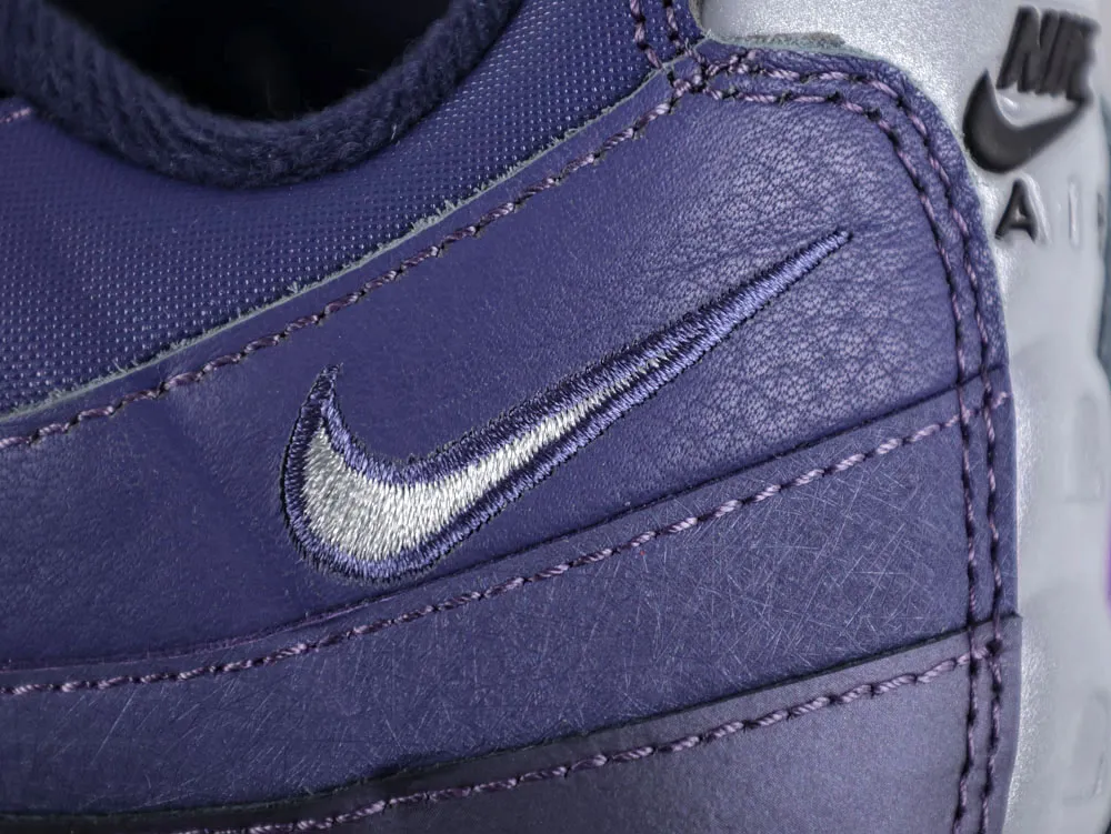 Close-up of a purple leather and fabric shoe with a silver embroidered logo.